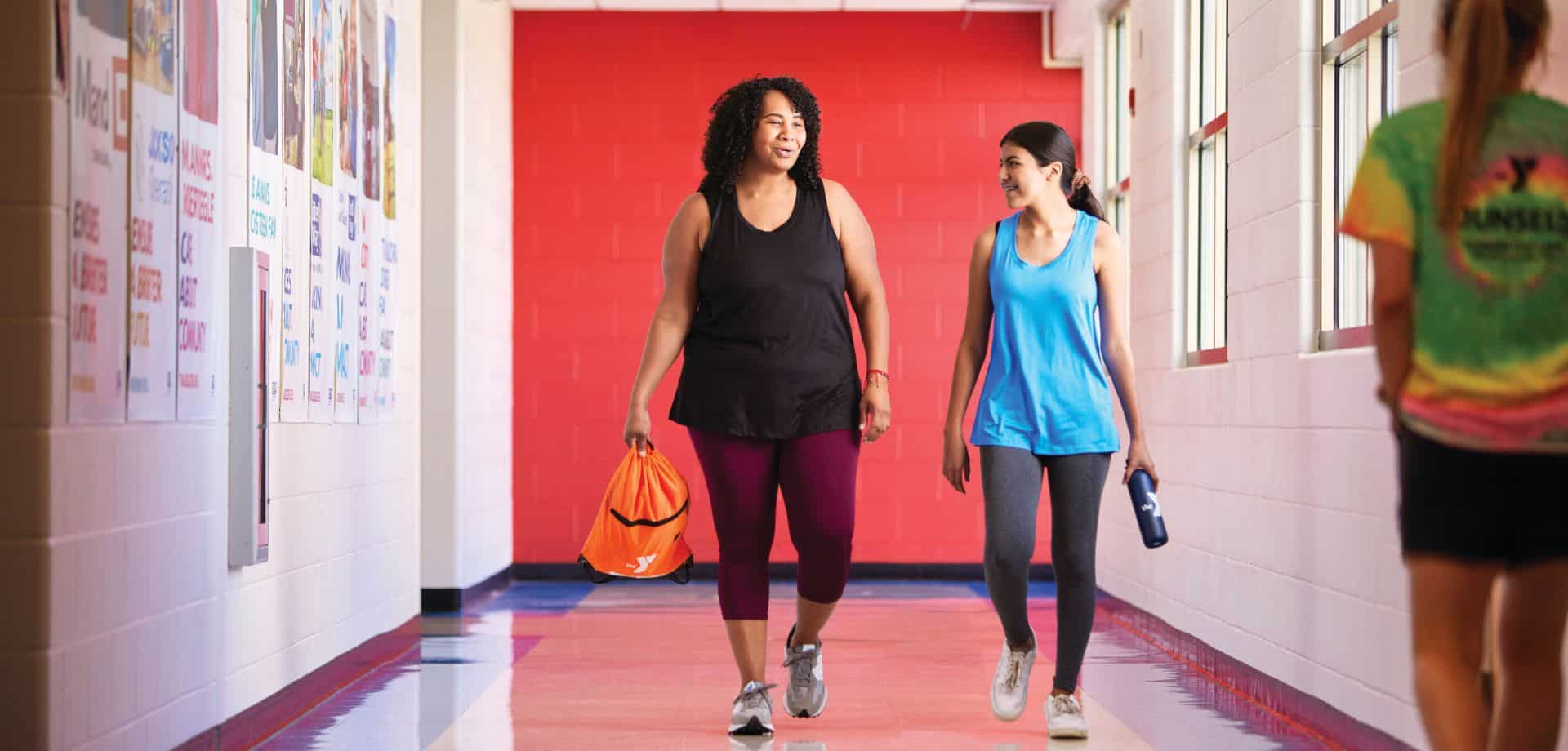 two ladies walking down a hallway in fitness attire