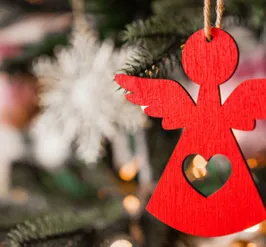 Red angel ornament with a cut out heart hanging on a Christmas tree