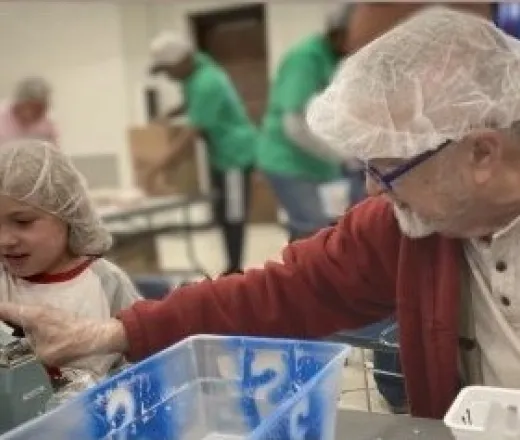 An adult man and a child volunteer together, packing food bags at a community rise against hunger event.