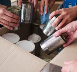image of peoples hands placing canned food into a cardboard box